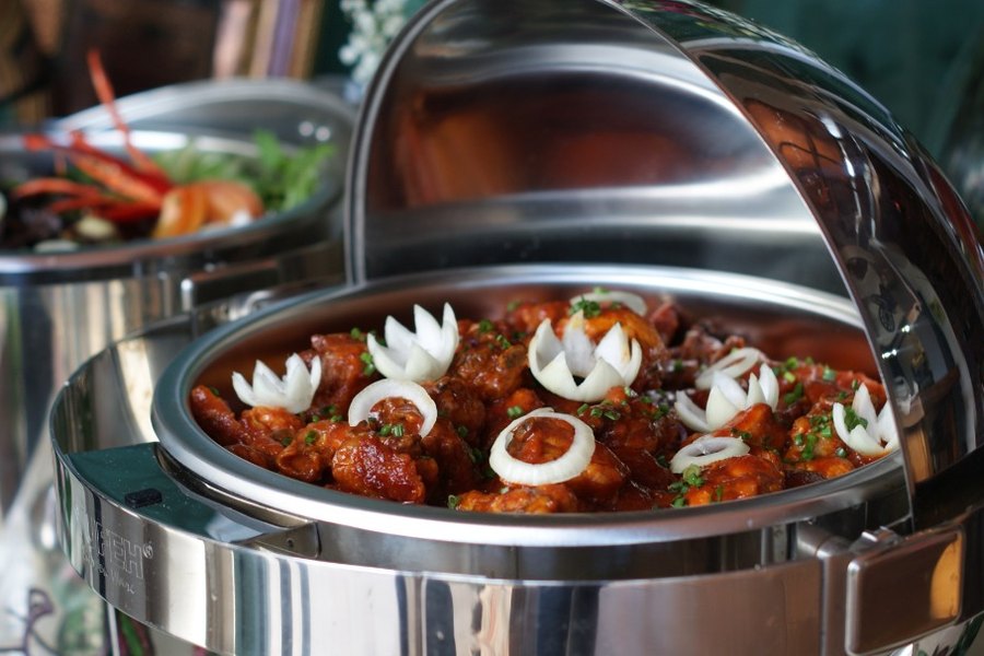 Sweet and sour chicken garnished with carved onion flowers in a chafing dish